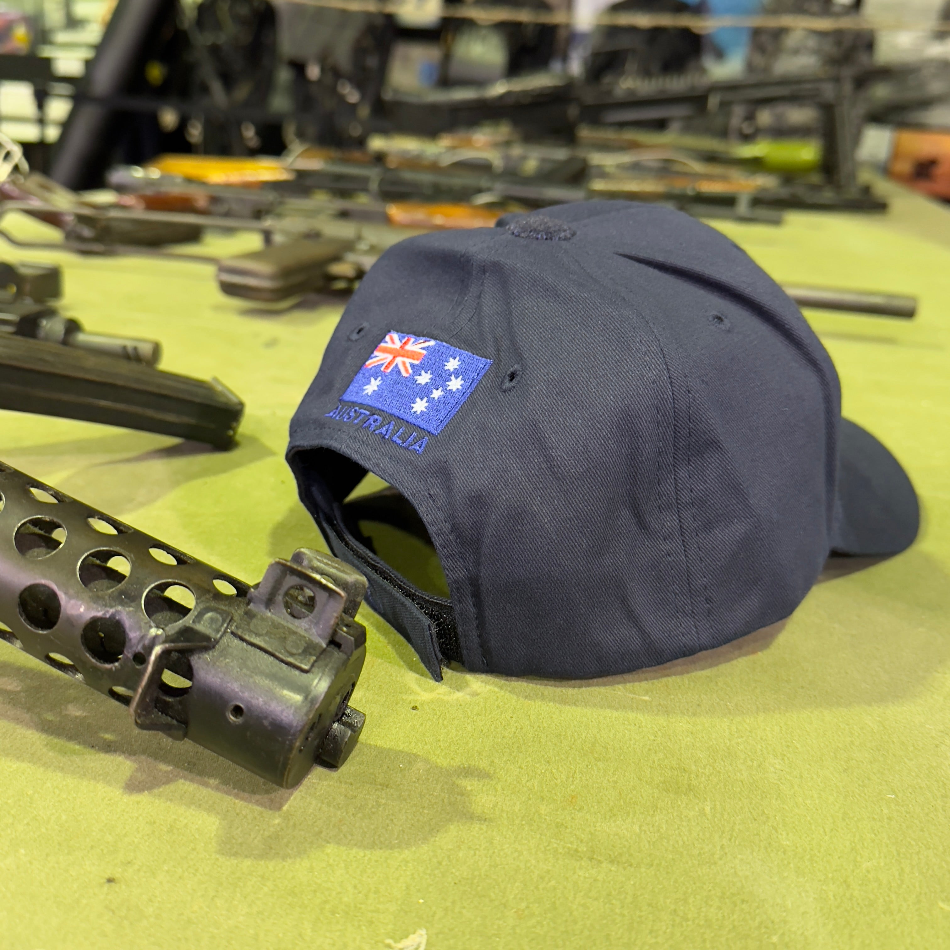 Ninesixfour Australian SAS cap in black with Australian flag patch displayed on a table with firearms