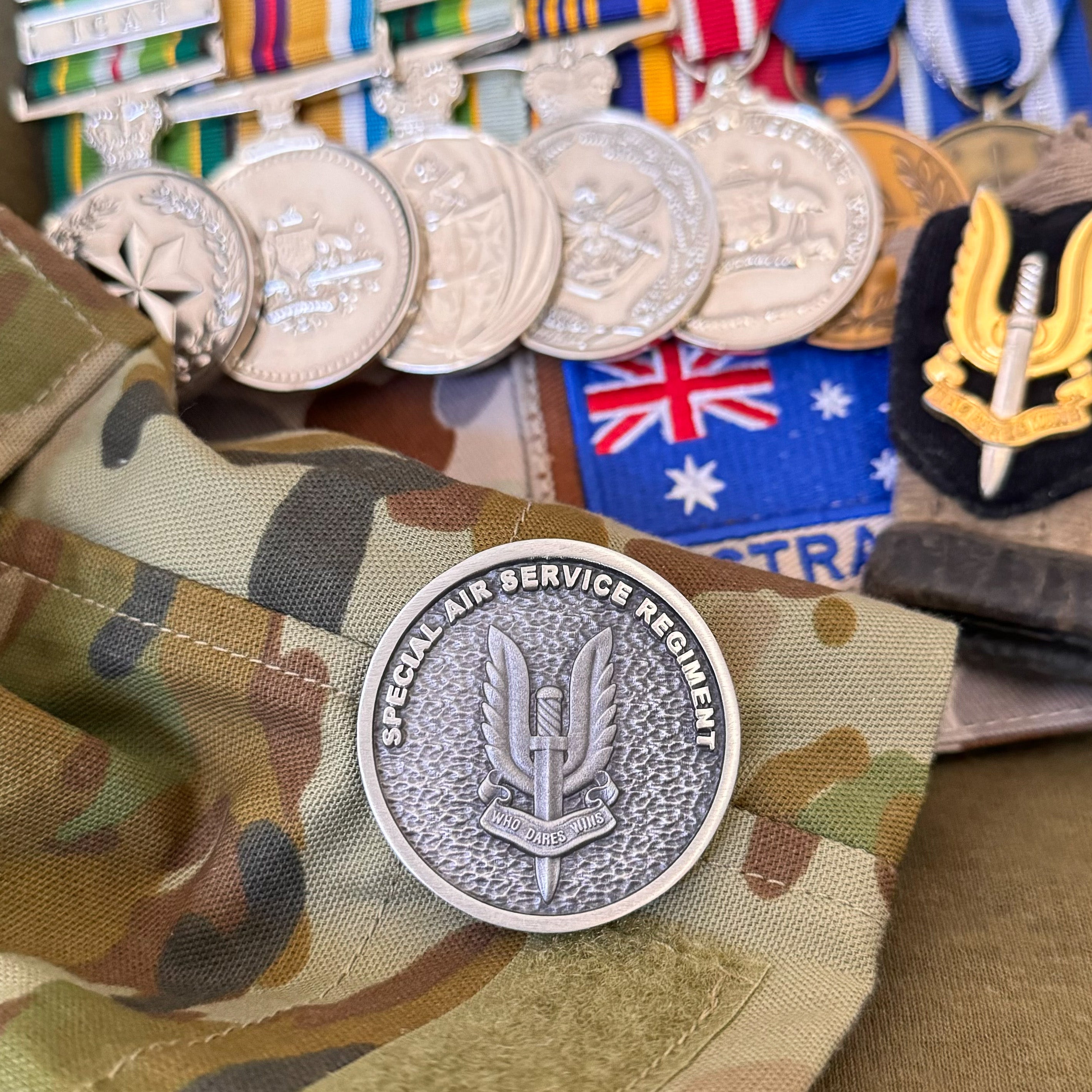 Australian SAS challenge coin on military camo fabric with medals and Australian flag patch in background