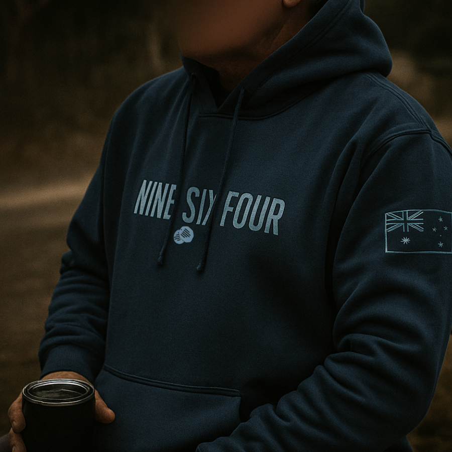 Man wearing NINESIXFOUR official SAS merchandise hoodie in dark blue with logo and flag patch holding a Yeti cup