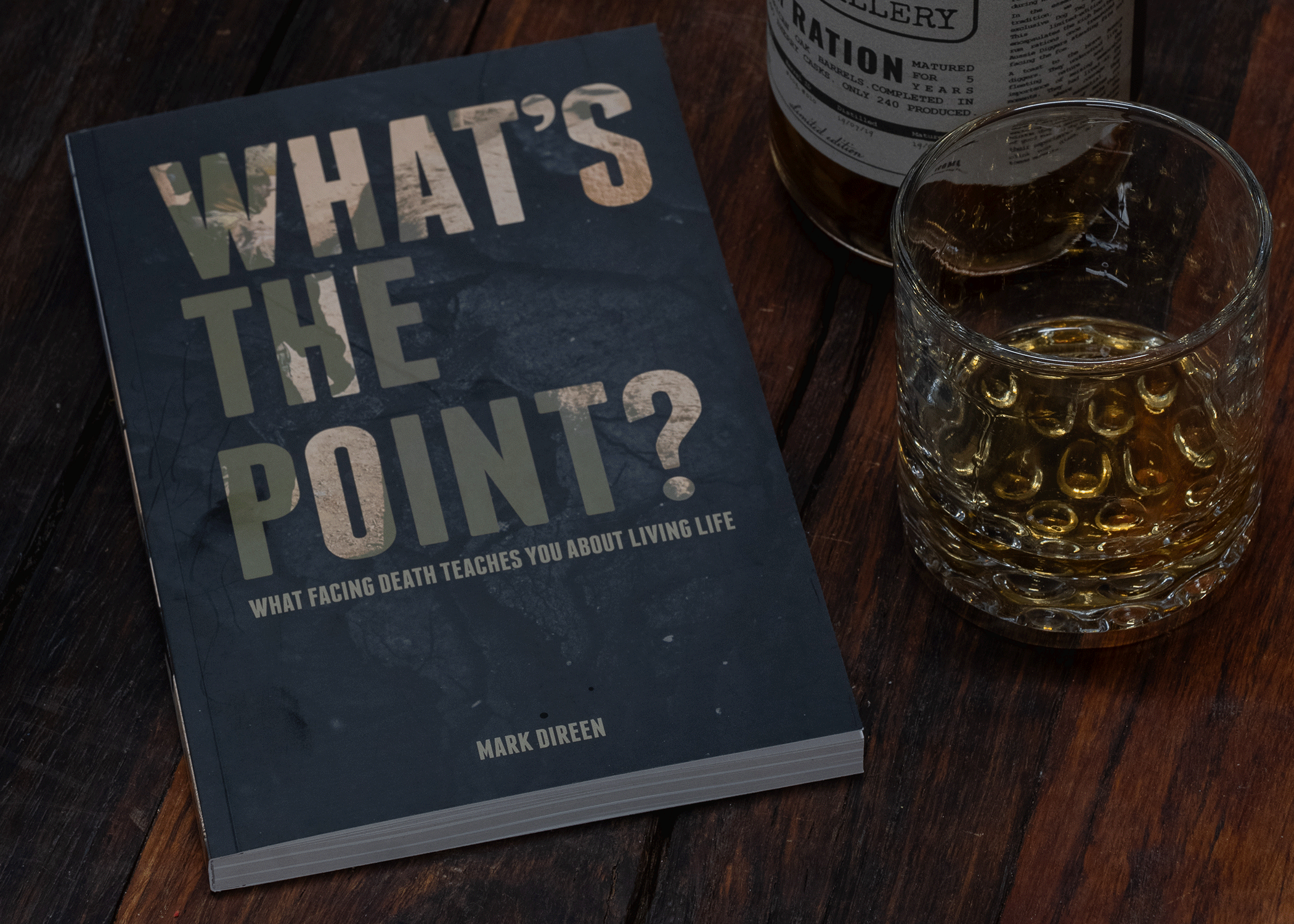 Signed SAS book titled What's the Point by Mark Dikeen on wooden table next to glass of whiskey
