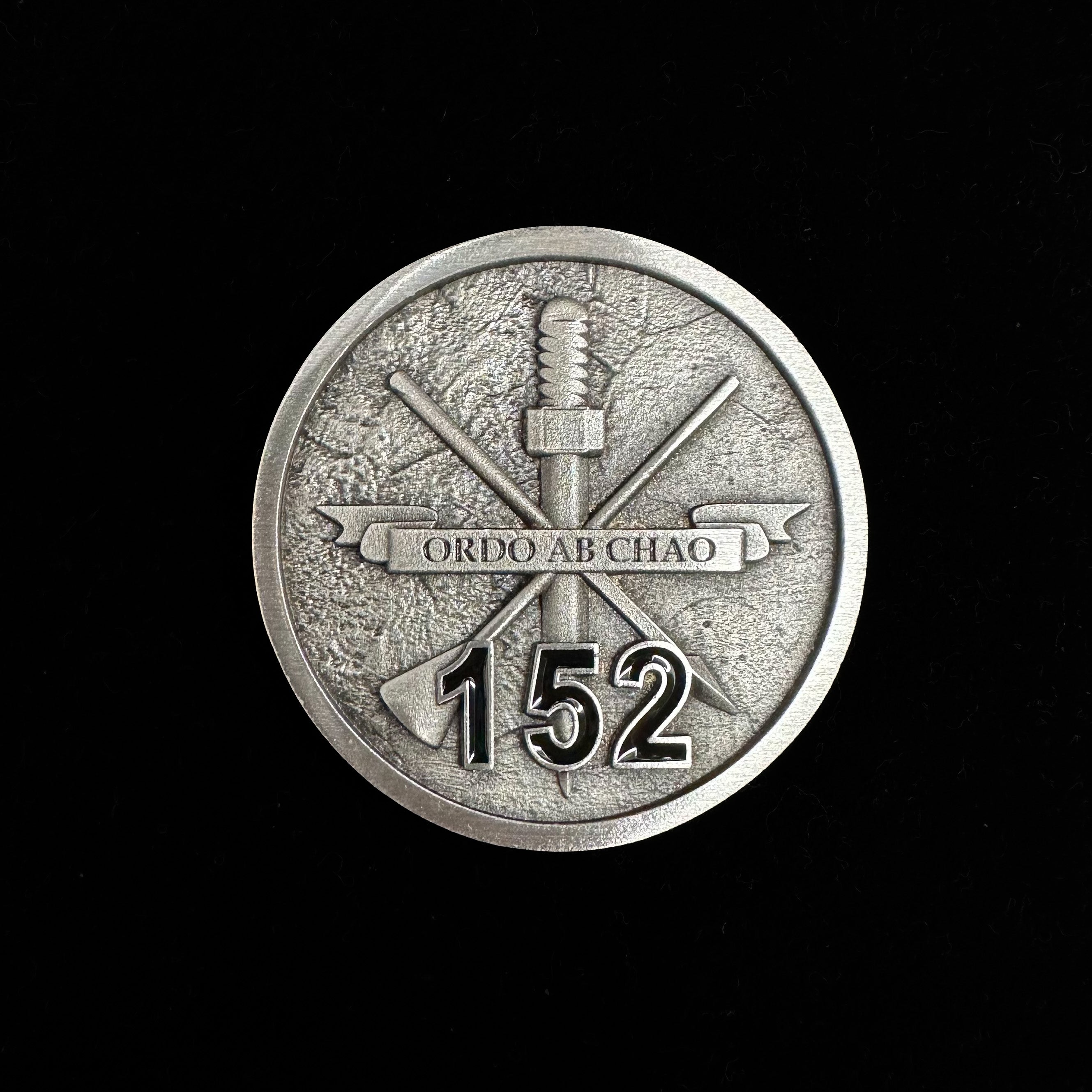 ninesixfour metal challenge coin with Ordo Ab Chao banner and number 152 on textured surface