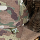 Close-up of a camouflage baseball cap with a small green 'NINE SIX FOUR' brand tag on the brim, layered over a tan fleece and CAMO mesh.