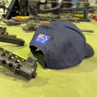 Ninesixfour Australian SAS cap in black with Australian flag patch displayed on a table with firearms
