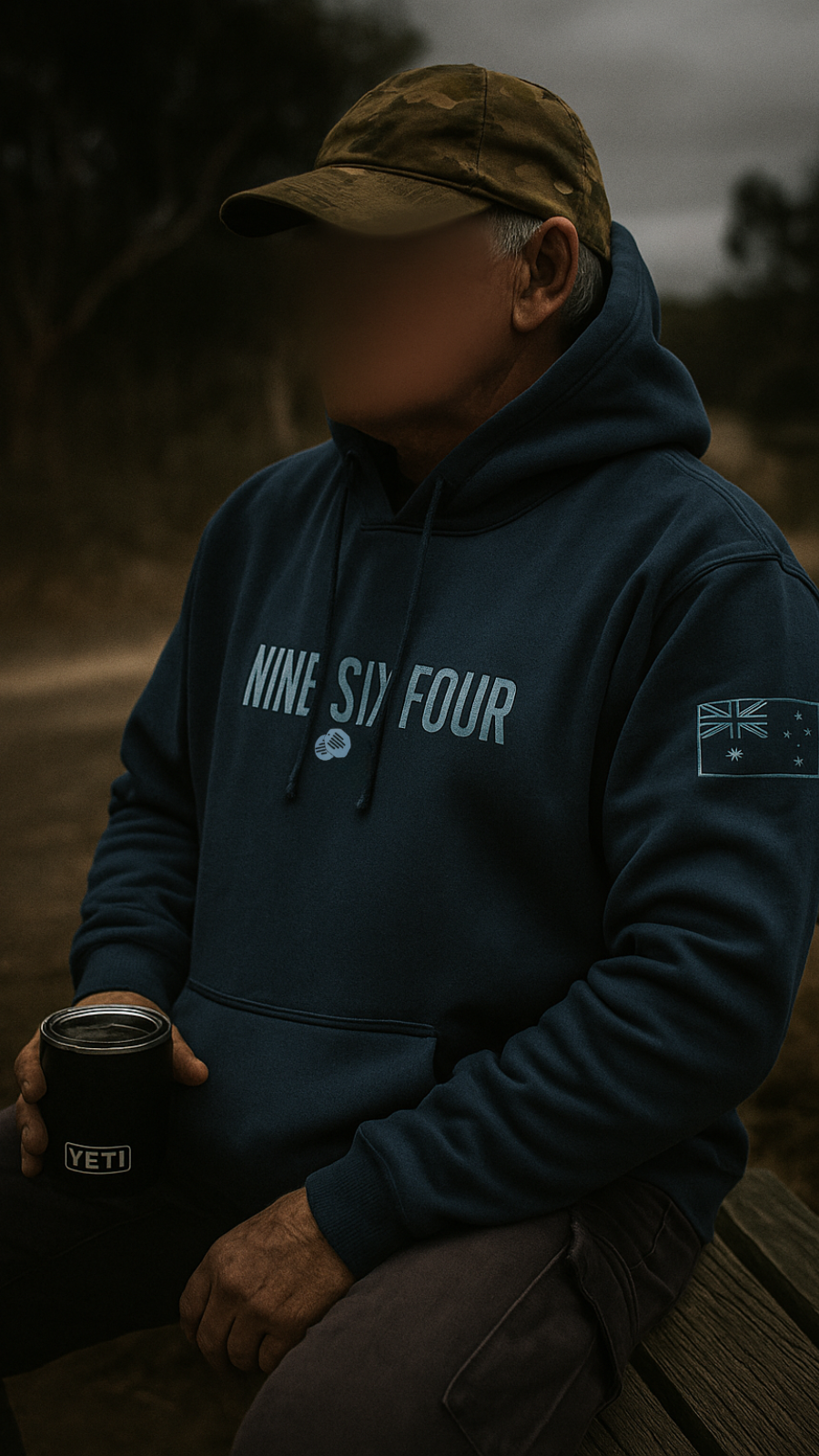 Man wearing NINESIXFOUR official SAS merchandise hoodie in dark blue with logo and flag patch holding a Yeti cup