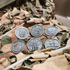 Set of six metal military challenge coins with various insignias displayed on camouflage fabric